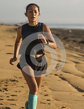 Outdoors fitness portrait of young attractive and athletic Asian Indonesian woman in her 40s running on the beach doing intervals