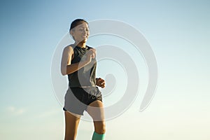 Outdoors fitness portrait of young attractive and athletic Asian Indonesian woman in her 40s running on blue sky background