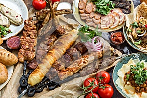 Outdoors Food Concept. Appetizing barbecued steak, sausages and grilled vegetables on a wooden picnic table.