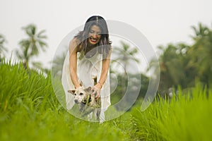 Outdoors holidays portrait of attractive and happy Asian woman in white dress enjoying beauty of nature walking her dog at