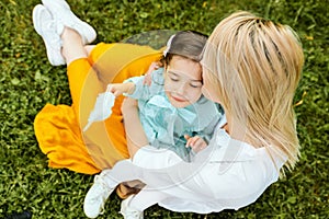 Outdoors image of beautiful mother kissing and cuddling with her daughter, enjoying the time together.