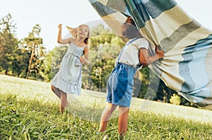 Outdoors image of children playing under the blanket, jumping and dancing together. Happy little boy and little girl enjoying