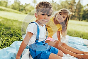 Outdoors image of happy children playing on the blanket outdoors. Little boy and cute little girl relaxing in the park. Adorable