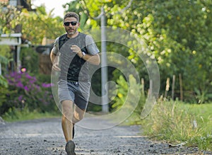 Outdoors jogging workout - young attractive and happy man in sport clothes and sunglasses running in city park enjoying fitness in