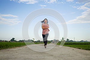 Outdoors jogging workout - young happy and dedicated Asian Chinese woman running at beautiful ccountryside road under a blue sky