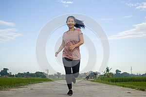 Outdoors jogging workout - young happy and dedicated Asian Korean woman running at beautiful ccountryside road under a blue sky on