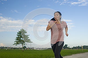 Outdoors jogging workout - young happy and dedicated Asian Korean woman running at beautiful ccountryside road under a blue sky on