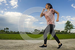 Outdoors jogging workout - young happy and dedicated Asian Korean woman running at beautiful ccountryside road under a blue sky on