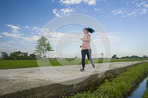 Outdoors jogging workout - young happy and dedicated Asian Korean woman running at beautiful ccountryside road under a blue sky on