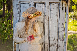 Outdoors lifestyle close up portrait of charming blonde young woman wearing a wreath of autumn leaves. Wearing stylish