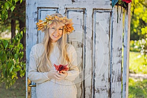 Outdoors lifestyle close up portrait of charming blonde young woman wearing a wreath of autumn leaves. Wearing stylish