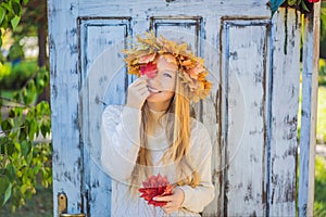 Outdoors lifestyle close up portrait of charming blonde young woman wearing a wreath of autumn leaves. Wearing stylish