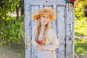 Outdoors lifestyle close up portrait of charming blonde young woman wearing a wreath of autumn leaves. Wearing stylish