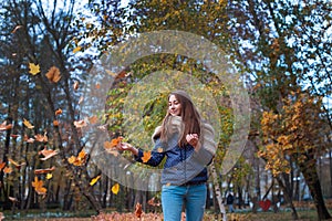 Outdoors lifestyle fashion image of happy beautiful girl throwing leaves up in the air in autumn park