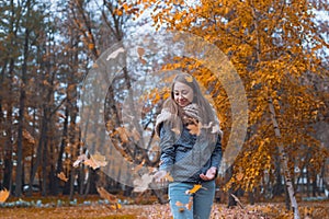 Outdoors lifestyle fashion image of happy beautiful girl throwing leaves up in the air in autumn park