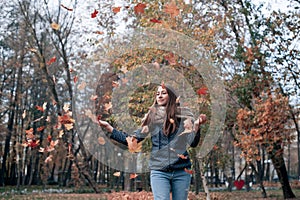 Outdoors lifestyle fashion image of happy beautiful girl throwing leaves up in the air in autumn park