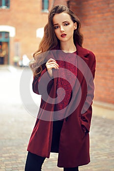 Outdoors lifestyle fashion portrait of brunette girl. Wearing stylish red coat. Walking to the city street. Long curly light hair.