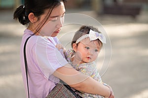 outdoors lifestyle portrait of Asian Chinese woman holding beautiful and adorable baby girl smiling cheerful on playground wearing