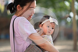 outdoors lifestyle portrait of Asian Chinese woman holding beautiful and adorable baby girl smiling cheerful on playground wearing