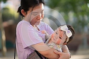 outdoors lifestyle portrait of Asian Chinese woman holding beautiful and adorable baby girl smiling cheerful on playground wearing