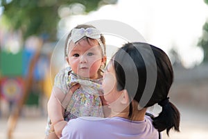 outdoors lifestyle portrait of Asian Chinese woman holding beautiful and adorable baby girl smiling cheerful on playground wearing