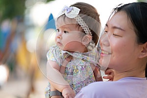 outdoors lifestyle portrait of Asian Chinese woman holding beautiful and adorable baby girl smiling cheerful on playground wearing