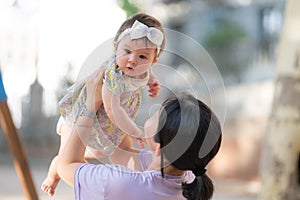 outdoors lifestyle portrait of Asian Chinese woman holding beautiful and adorable baby girl smiling cheerful on playground wearing