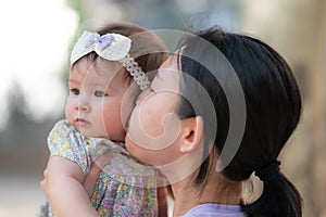 outdoors lifestyle portrait of Asian Chinese woman kissing beautiful and adorable baby girl smiling cheerful on playground wearing