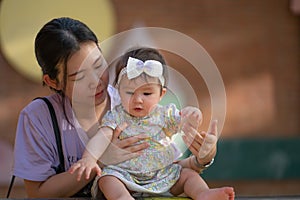 outdoors lifestyle portrait of Asian Chinese woman playing with beautiful and adorable baby girl smiling cheerful on playground