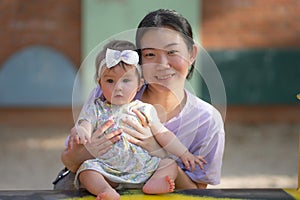 outdoors lifestyle portrait of Asian Chinese woman playing with beautiful and adorable baby girl smiling cheerful on playground