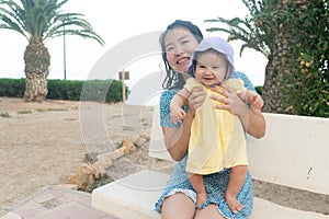 outdoors lifestyle portrait of Asian mother and her little daughter - beautiful woman holding his adorable and happy baby girl at