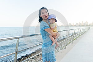 outdoors lifestyle portrait of Asian mother and her little daughter - beautiful woman holding his adorable and happy baby girl at