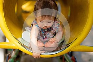outdoors lifestyle portrait of beautiful and adorable 9 month old baby girl sitting on yellow tube at children playground in city
