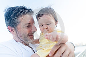 outdoors lifestyle portrait of father and little daughter - man holding his adorable and happy baby girl in front of the see