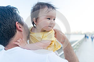 outdoors lifestyle portrait of father and little daughter - man holding his adorable and happy baby girl in front of the see