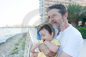 outdoors lifestyle portrait of father and little daughter - man holding his adorable and happy baby girl in front of the see