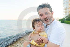 outdoors lifestyle portrait of father and little daughter - man holding his adorable and happy baby girl in front of the see