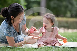 outdoors lifestyle portrait of mother and daughter - young happy and sweet Asian Korean woman playing with her 8 months baby girl