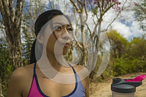 Outdoors lifestyle portrait of young attractive tired and thirsty Asian woman drinking water after hard running workout cooling