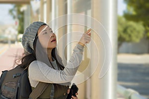 Outdoors lifestyle portrait of young beautiful and happy Asian Korean woman waiting the train on station platform bench checking