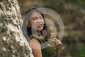 Outdoors lifestyle portrait of young cool Asian Korean woman in green Summer dress  holding sunglasses biting them playful and