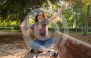 Outdoors lifestyle portrait of young happy and beautiful Asian Korean woman enjoying relaxed and cheerful at sitting on city park