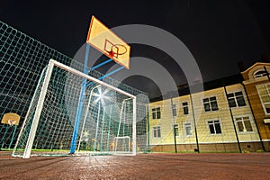 Outdoors mini football and basketball court with ball gate and basket surrounded with high protective fence brightly illuminated