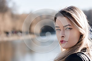 Outdoors portrait of beautiful young brunette girl. Woman smiling happy on sunny summer or spring day outside on city background.