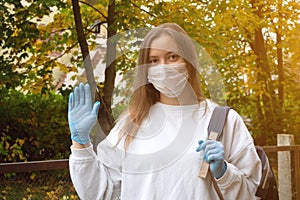 Outdoors portrait of beautiful young woman wearing cotton white mask and medicalgloves greeting and say hello, Nature and trees in