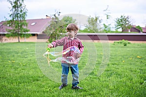 Outdoors portrait of cute preschool boy blowing soap bubbles on a green lawn at the playground