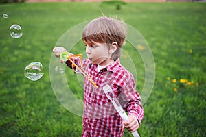 Outdoors portrait of cute preschool boy blowing soap bubbles on a green lawn at the playground