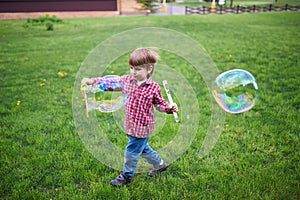 Outdoors portrait of cute preschool boy blowing soap bubbles on a green lawn at the playground