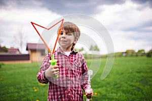 Outdoors portrait of cute preschool boy blowing soap bubbles on a green lawn at the playground