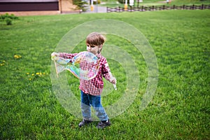 Outdoors portrait of cute preschool boy blowing soap bubbles on a green lawn at the playground